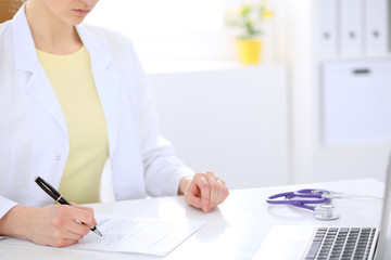 Close-up of a female doctor filling  out application form , sitting at the table in the hospital