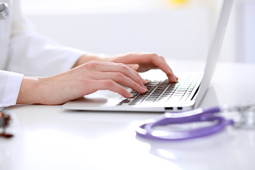Close-up of female doctor typing laptop sitting at a table in the hospital