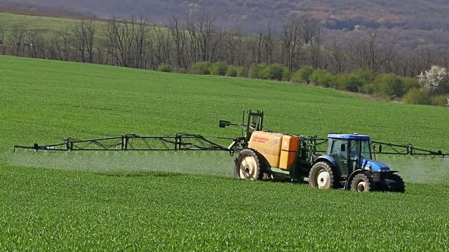 Tractor spraying field, rural landscape in countryside