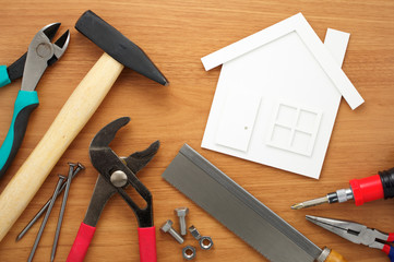 Home planning and preparing.
House shaped paper cutout and tools on wooden table.
