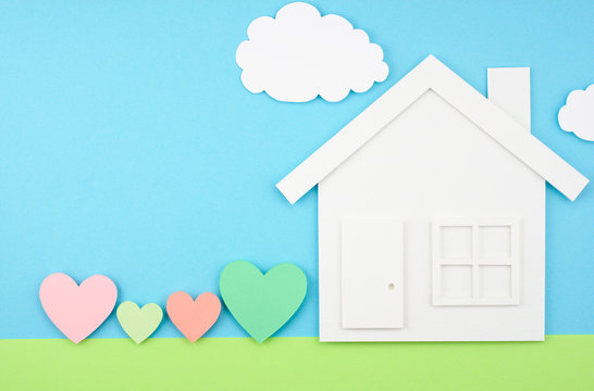 House and hearts on paper background.
House shaped paper cutout and four hearts on sky and grass field made of paper.
