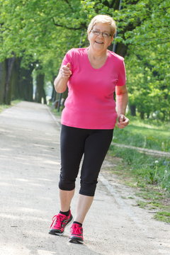 Senior woman running in sunny park, jogging outside, healthy lifestyle