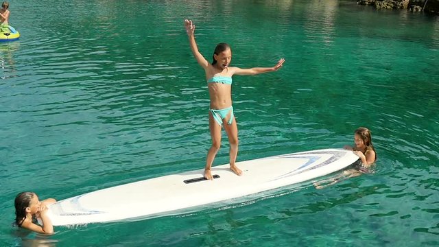 Teenage girl try to stay on surf while other two swinging the board
