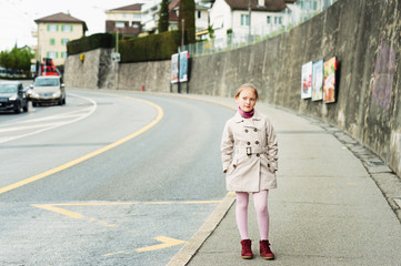 Outdoor portrait of a cute little girl, wearing beige coat and red shoes