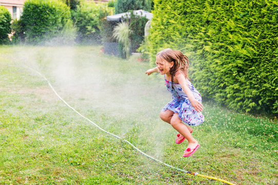 Child playing with garden sprinkler, jumping over