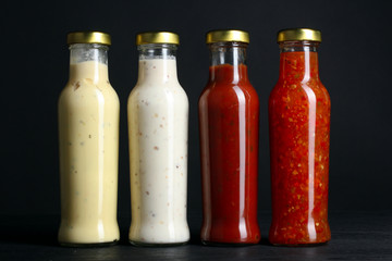 a variety of sauces in glass bottles on a black wooden background