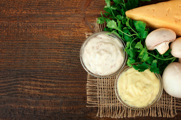 sauces in a glass bowl near the leaves of greens with cheese and mushrooms on a brown wooden background
