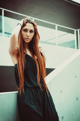 Obraz premium Red-haired girl model standing near the stairs in a modern architectural environment.