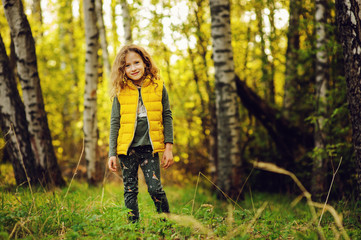 happy child girl in yellow vest walking in summer sunny forest. Kids exploring nature. Cozy rural scene