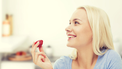 happy woman eating strawberry on kitchen