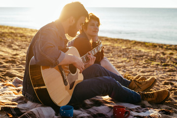 young caucasian couple playing guitar on beach at sunset - Powered by Adobe