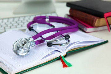 Stethoscope lying on a notebook computer in the background and books