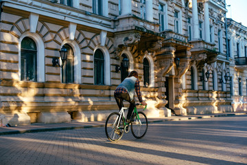 young brunette man riding fixed-gear bicycle in the city on a sunny day