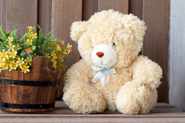 Teddy bear doll with artificial flowers at wooden wall background 