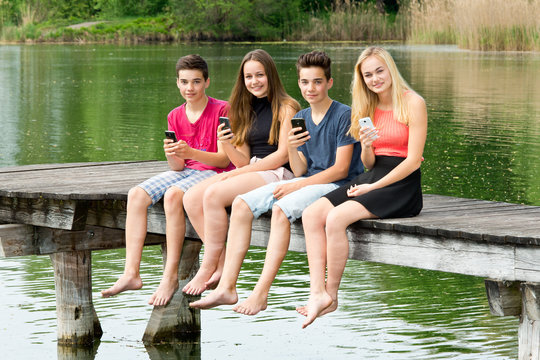 Vier Teenager / Jugendliche mit Smartphone draußen in der Natur