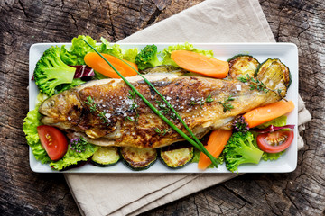 Grilled trout with vegetables on wooden background