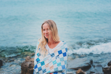 young woman in cozy quilt blanket relaxing on the beach in summer
