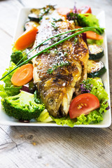Grilled trout with vegetables on wooden background