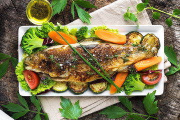 Grilled trout with vegetables on wooden background