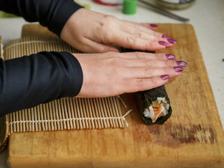 Woman rolling sushi on a cutting board.