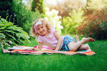Naklejka na ściany i meble cute child girl reading book in summer garden outdoor. Kids learning on summer vacations.