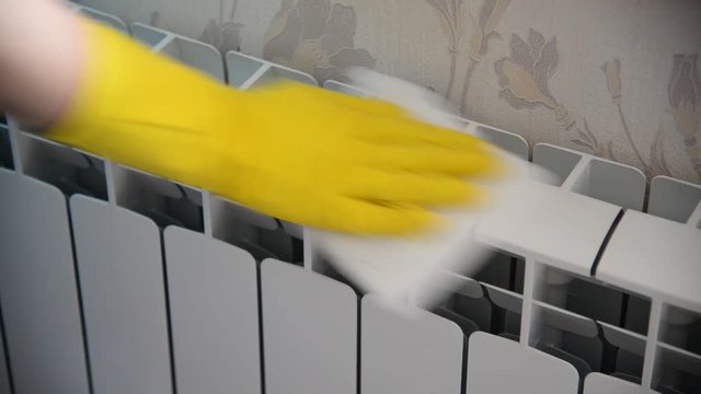 Female hand in  rubber glove cleans heating radiator