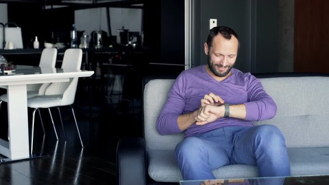 Young happy man with smartwatch sitting on sofa at home
