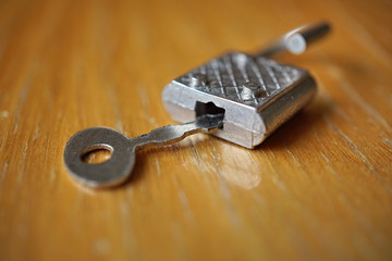 Small metal key opening or closing an silver lock on the wooden surface 