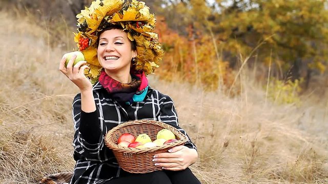 beautiful young girl with a basket of ripe apples   / beautiful young girl in a wreath of leaves with a basket of ripe apples, autumn background 