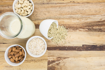 Plant based milk and and bowls with ingredients, on wooden background