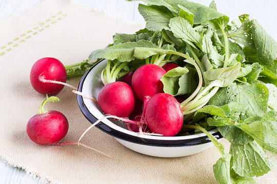  Fresh radishes.   Fresh radishes in a white bowl on a napkin on a light wooden background.