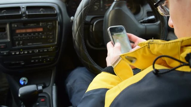 Young driver looking at map on smart phone while sitting in the car. He searching the right route to continue his travel