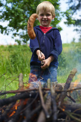 Cute boy cooking sausage by bonfire