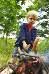 Cute boy cooking sausage by bonfire
