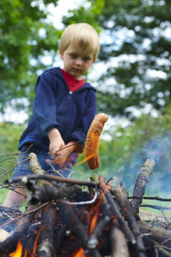 Cute boy cooking sausage by bonfire