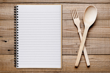 Cookbook, fork and spoon on wooden table top view