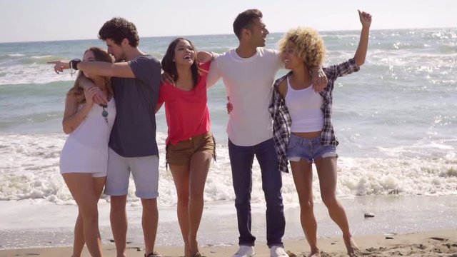 Five young attractive people posing in front of camera on the beach and have a great time.