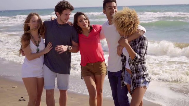 Group of young attractive people standing in front of camera on the beach and have a great time in slow motion.