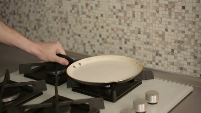 Cooking breakfast - man with smartphone in the kitchen to fry egg in a frying pan on  gas stove