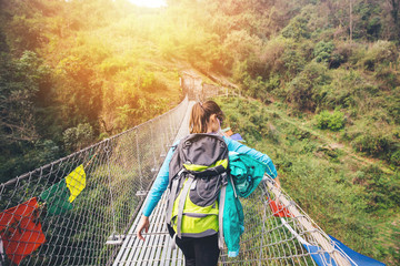 Female hiker crossing suspension footbridge and touching prayer flags