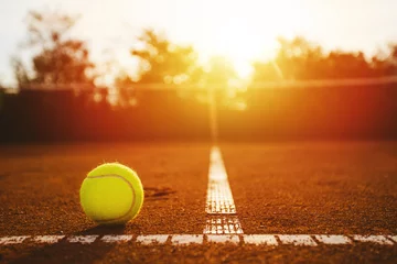 Wandaufkleber Tennis ball on clay court at suset © yossarian6