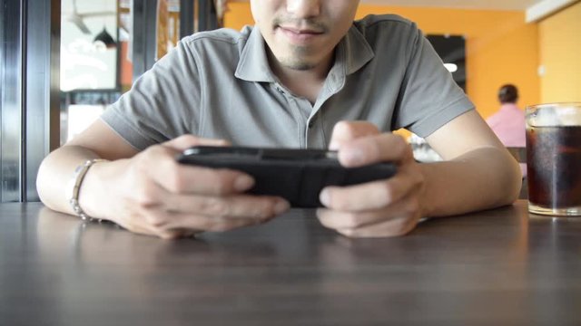 Handsome Asian male use smartphone with touch screen for play a game in restaurant with cola drink nearby HD