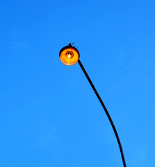 City street lighting lamp lit at dusk on a long pole. Photo on blue cloudless sky in the evenong