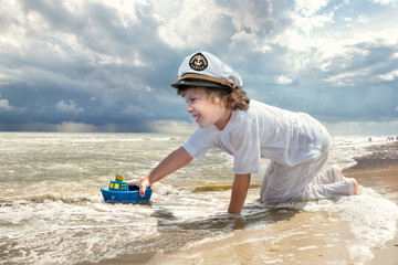 Little boy playing with toy ship on the beach at warm summer day