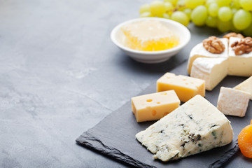 Glass of white wine and assorted cheese with grape on a stone and slate background.