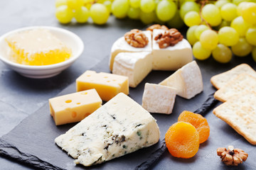 Glass of white wine and assorted cheese with grape on a stone and slate background.