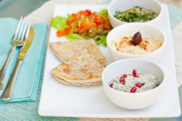 Assortment of dips: hummus, chickpea dip, tabbouleh salad, baba ganoush and flat bread, pita on a plate