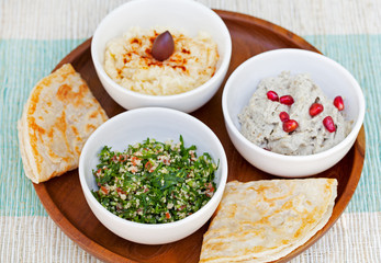 Assortment of dips: hummus, chickpea dip, tabbouleh salad, baba ganoush and flat bread, pita on a plate