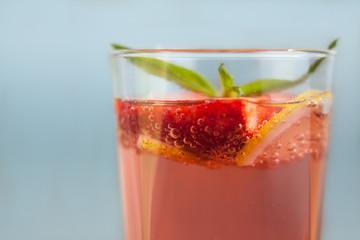 Glass of strawberry lemonade with pieces of strawberry, lemon and fresh mint. Closeup of mojito with beach on background. Fresh summer bright strawberry cocktail.