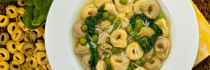 Tortellini Soup with Spinach and Peas. Panoramic image. Selective focus.